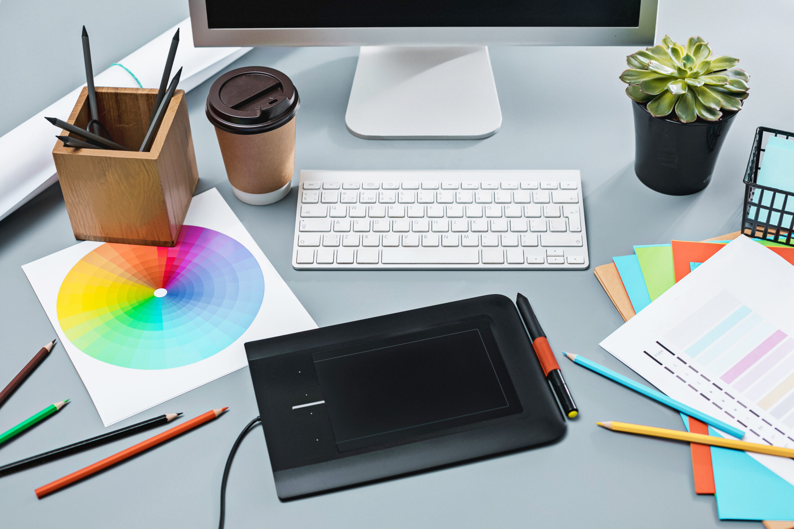 The desk with laptop, notepad with blank sheet, pot of flower, stylus and tablet for retouching. Workspace of professional retoucher. Creativity, design, art and modern equipments concept